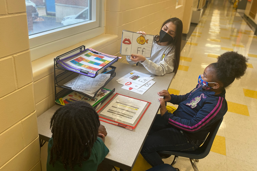 Tutor goes over the letter "f" with two students at a table